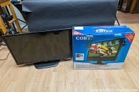 LG 32 inch flatscreen TV and COBY 22 inch monitor in original box shown side by side on hardwood floor.