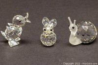 Three Swarovski crystal figurines: baby duckling, rabbit, and snail on black background.
