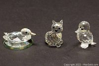 Three Swarovski crystal figurines on dark background showing a baby duckling on mirrored base, a mouse with metal tail, and a duckling.
