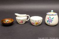 Four items side by side: Moorcroft bowl in brown/orange floral glaze, Royal Crown Derby creamer and sugar bowl with floral patterns and gold trim, and Poole Pottery lidded sugar bowl with painted flowers.