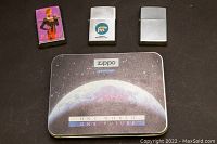 Four vintage Zippo lighters and original Millennium Edition tin box arranged on a black surface.