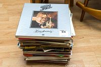 Stack of assorted vinyl records with Louis Armstrong album on top, showing album title and artist