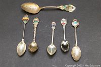 Top view of 6 sterling silver collector spoons laid out with enamel crests and different bowl inscriptions visible.