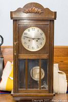 Full view of the wooden wall clock with beveled glass and carved floral detail on top.