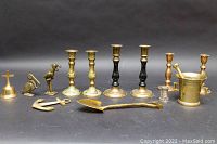 Full view of brassware collection including candleholders, bird figurines, anchor, bell, thimble, mortar and pestle, and scoop