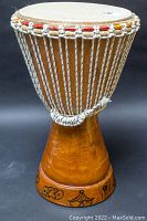 Front view of handcrafted African djembe drum showing natural wooden body, rope tuning system, and decorated base.