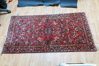 Full view of red wool rug on wood floor, showing overall size and pattern.