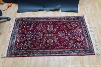 Full view of rectangular red wool rug laid on wood floor