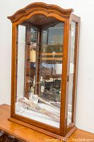 Full front and side view of the wooden curio cabinet showing the mirrored back and glass shelves, placed on a table.