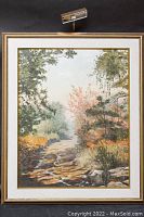 Front view of framed oil painting showing forest path and overhead light attached to frame.