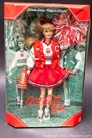 Front view of Mattel Collector's Edition Coca-Cola Barbie doll in original box, showing doll in cheerleader outfit with pom-pom, megaphone and varsity jacket, box has minor wear.