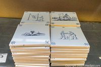 Stacked vintage Delft-style wall tiles showing various illustrations such as children playing and workers by the sea, confirming quantity and condition.
