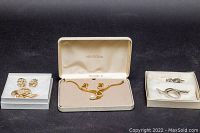 Overview of all costume jewelry sets displayed in boxes with black background. From left to right: Boucher and Trifari brooches and clip-on earrings, Vendome necklace and earrings with the original box.