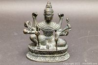 Front view showing the goddess seated with four arms visible on each side holding weapons and ornaments, detailed headdress and armor scales pattern on torso.