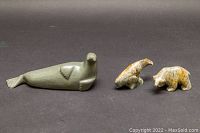 Three soapstone carvings on a dark background: one larger sea lion and two smaller carvings of a beluga whale and a bear.