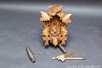 Front view of vintage REGULA cuckoo clock with pine cone weights and wooden pendulum attached by chains to clock mechanism.
