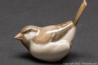 Porcelain bird figurine side profile on dark surface showing smooth glossy finish, natural color palette and delicate details.