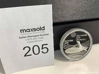Photo of coin standing upright in plastic capsule with seller information card beside it.