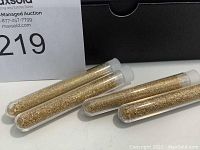 Four plastic test tubes containing 24k gold flakes seen from an angle with lot number in background.