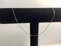 Thin sterling silver necklace displayed on a black velvet necklace stand.
