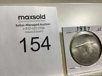 1967 Canadian silver dollar coin in a white cardboard holder, showing the flying goose design on the reverse side.