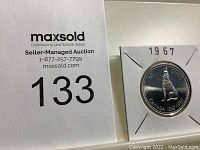 Front side of 1967 Canadian silver half dollar coin displayed in a white protective holder with the year 1967 marked on it. Shows a howling wolf design and inscriptions 'CANADA 1867-1967' and '50 CENTS'.