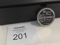 Photo of coin in its black box with auction number card visible, showing the coin's face with diver image and Olympic text.