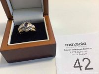 Ring displayed inside a polished wooden box with black velvet base and white cushioning lid.