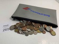 Gray zipper pouch with Bank of America logo partially open with world coins spilling out showing a variety of metallic coins.