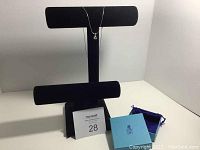 Necklace displayed on black stand with box and pouch on the side