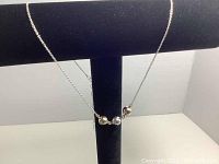 Necklace displayed on a black stand showing all three beads in gold, silver, and rose gold tones.