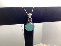 Close-up front view of necklace pendant showing the faceted pale green gemstone and smaller round green gemstone with detailed silver bezel.