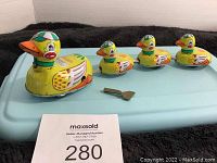 Four yellow tin toy ducks in varying sizes with a metal wind-up key on a blue surface