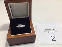 Sterling silver ring with clear stones on a black velvet cushion inside a wooden display box, accompanied by auction card.