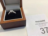 Front view of the silver-tone ring with square-cut center stone in wooden and velvet box.