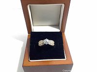 Gold tone ring with large clear rhinestone center and smaller rhinestones on band displayed in a brown wooden ring box with navy blue velvet interior.