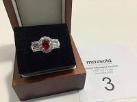 Ring displayed on black cushion inside a wooden box with auction tag nearby.