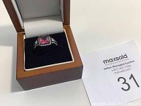 Ring displayed in brown box with black cushion interior, showcasing pink center stone and rhinestones on band.