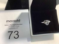 Silver 925 ring with knot design inside black jewelry box alongside lot number card