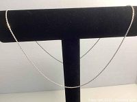 Silver necklace hung on a black jewelry display stand showing full length and chain detail.