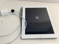 View of iPad showing Apple logo on screen with charger and cable beside it