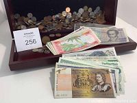Wooden box containing assorted coins and paper money, including banknotes featuring different countries and denominations.