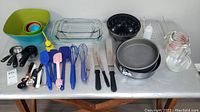 Shows full contents of assorted bakeware including mixing bowls, measuring cups, glass trays, cake pans, utensils, and a pitcher