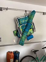 Green and blue striped foldable beach chair with attached umbrella hanging on the wall with two cup holders on the armrests.