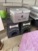 Photo of gray fabric box marked 'Dog Stuff' on top of two dark wooden dog toy storage boxes labeled 'Duncan Dog Toys'.