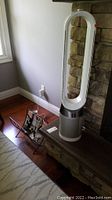 Front view of Dyson bladeless tower fan placed on hearth next to stone fireplace with magazine rack on floor.