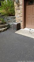 Two dark brown woven resin garden hose reels by Suncast next to a stone wall and garage door, hose extended on driveway.