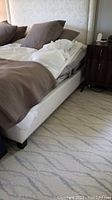 Full view of the bed with mattress, upholstered frame, and headboard from side angle. Bedding shows the mattress and pad.