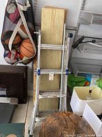 Folded Werner aluminum ladder leaning against wall with basketballs and other items around it.