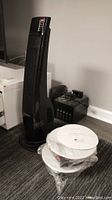 Black Lasko tower heater next to two wrapped white Leon ceiling speakers with cutout templates on a floor
